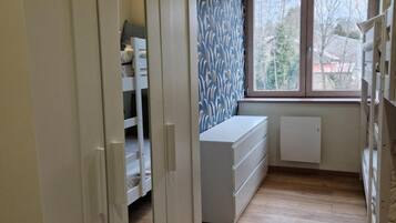 Een kamer met een kledingkast, een witte dressoir, een radiator en een raam met uitzicht op bomen.