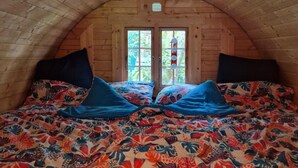Um quarto de sótão acolhedor, com paredes de madeira e teto inclinado, com uma cama grande e roupa de cama floral, e duas janelas.