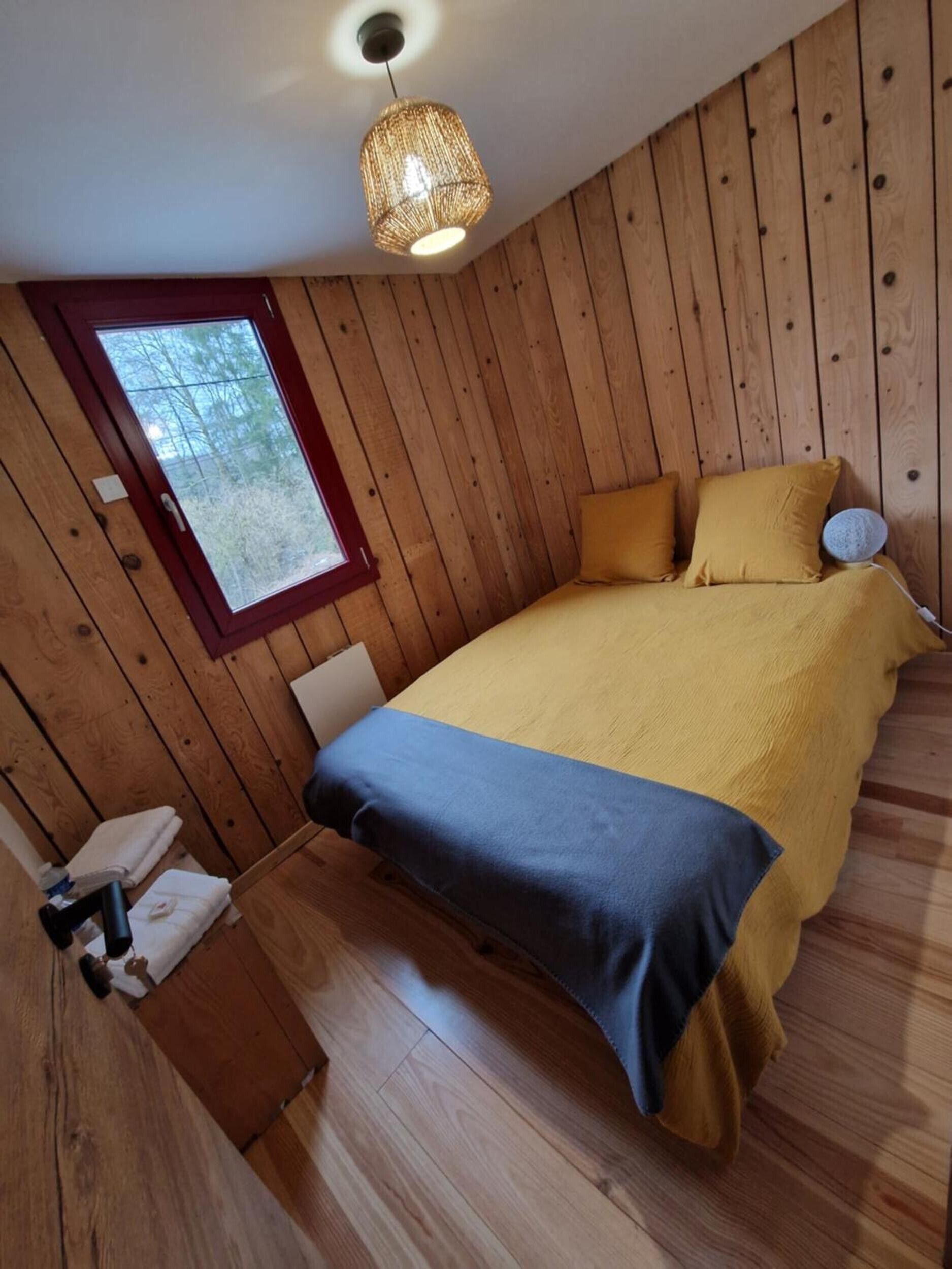 Una habitación con paneles de madera, una cama, un ventanal y una lámpara colgante.