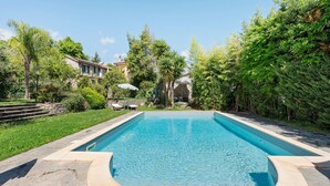 A rectangular swimming pool with a stone border, surrounded by lush greenery and a stone pathway.