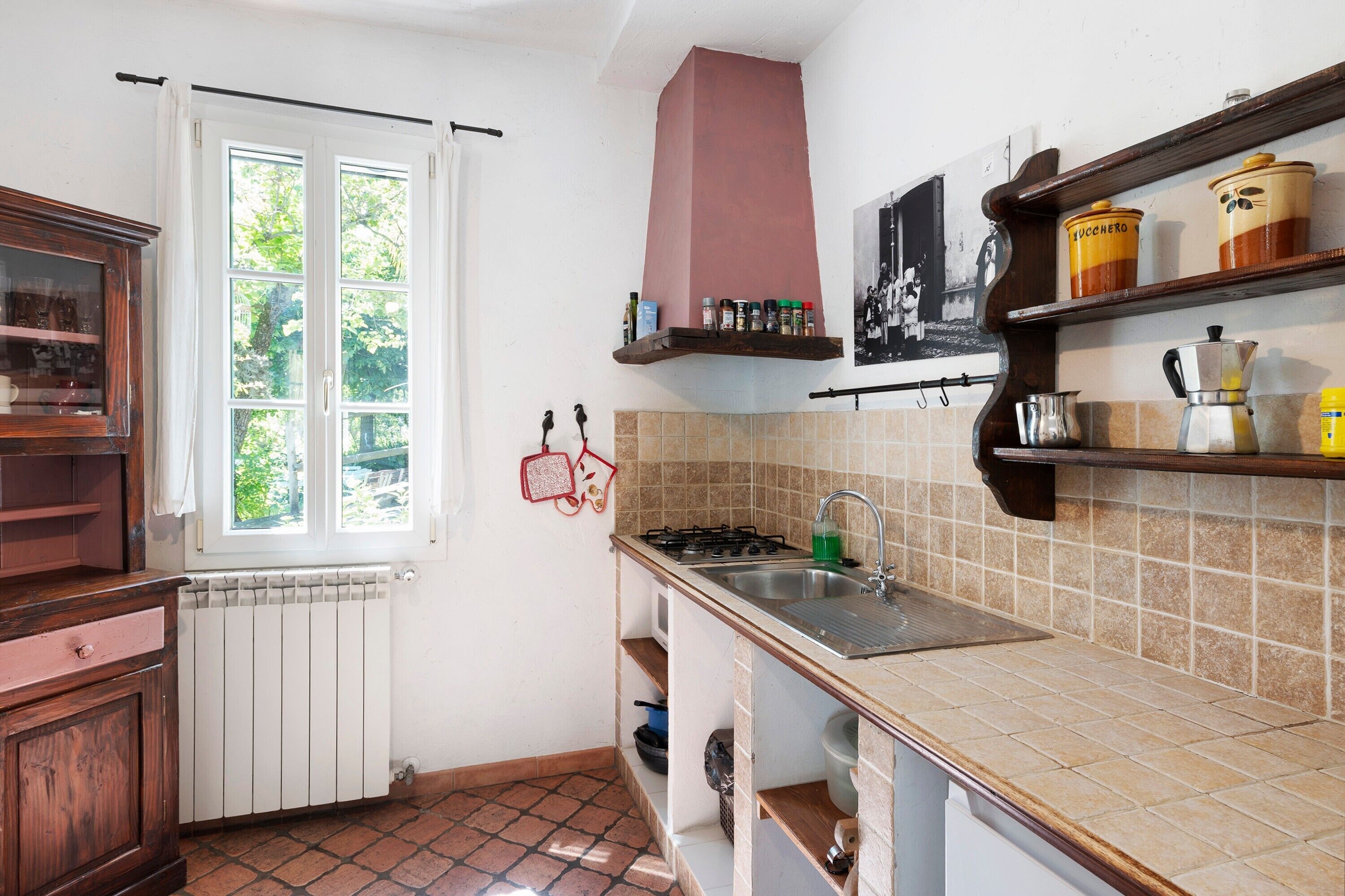 A kitchen with a window, a stove, a sink, and shelves with kitchenware.