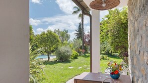 A balcony with a view of a garden, a table with chairs, and a vase with flowers.
