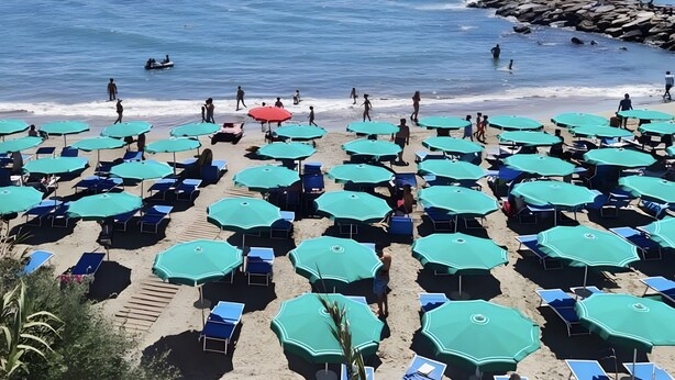 A beach with rows of sunbeds and umbrellas, a rocky shoreline, and the ocean in the background.
