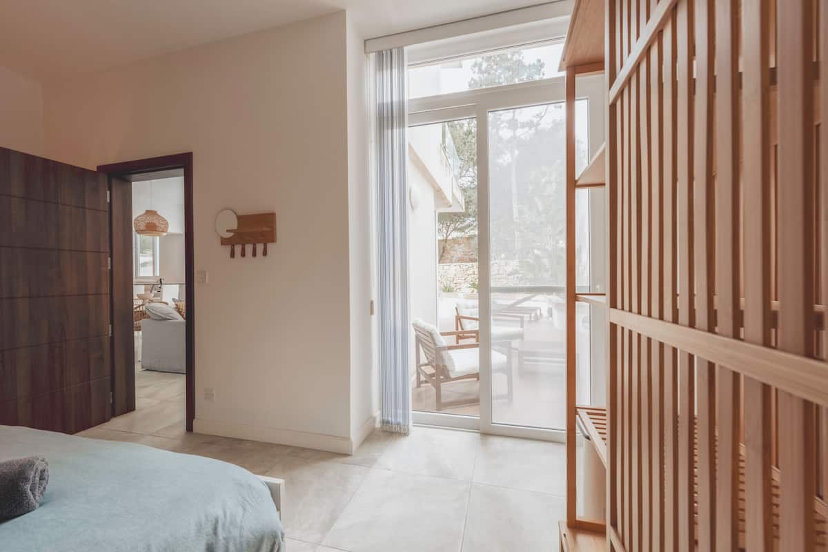 Habitación con cama, separador de madera, puerta corredera de vidrio a un área de estar exterior y un espejo pequeño sujeto a la pared.