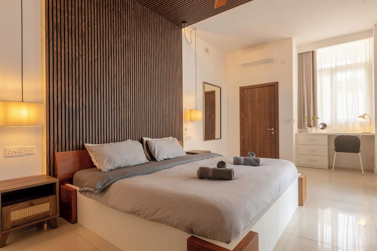 Un dormitorio moderno con una cama grande, mesitas de noche, un escritorio y una silla.
