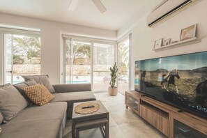 Una sala de estar moderna con sofá, televisor y vistas a una piscina y zona exterior.