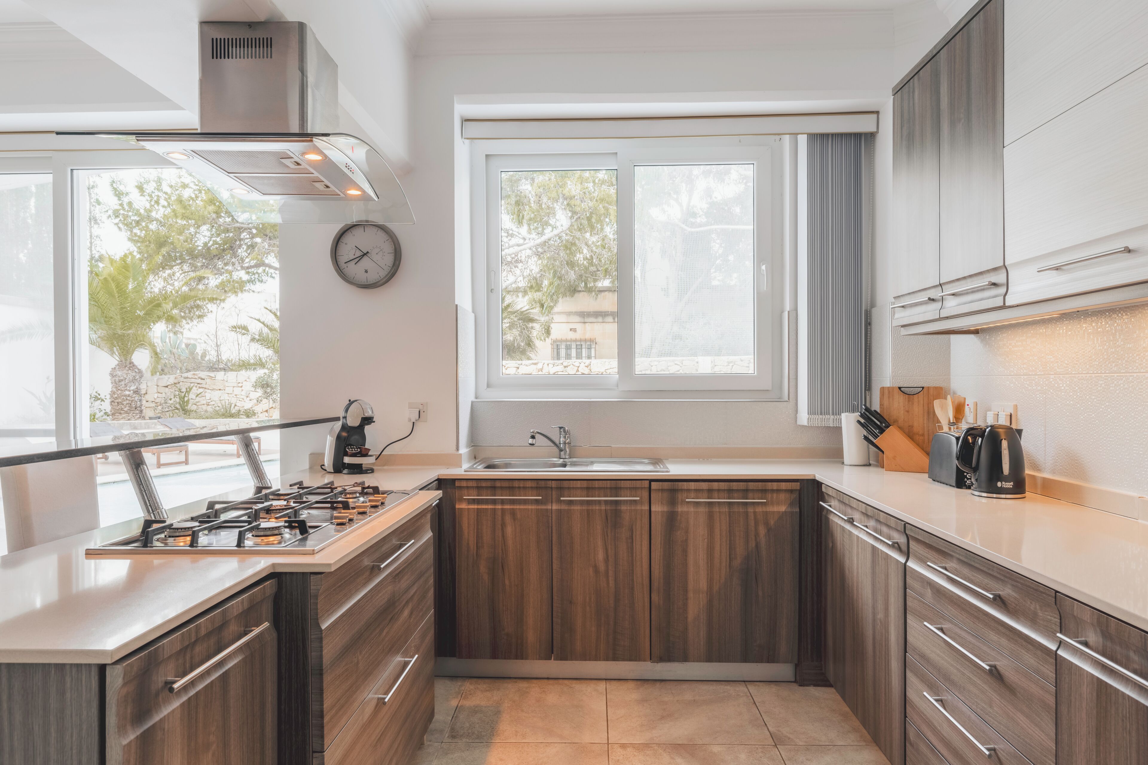 A kitchen with wooden cabinets, a gas stove, a sink, and a window with a view of trees.