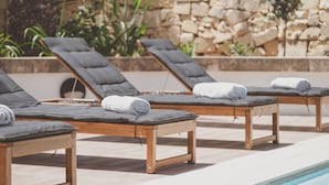 A poolside area with lounge chairs and a stone wall. - Villa Marni (Munxar)