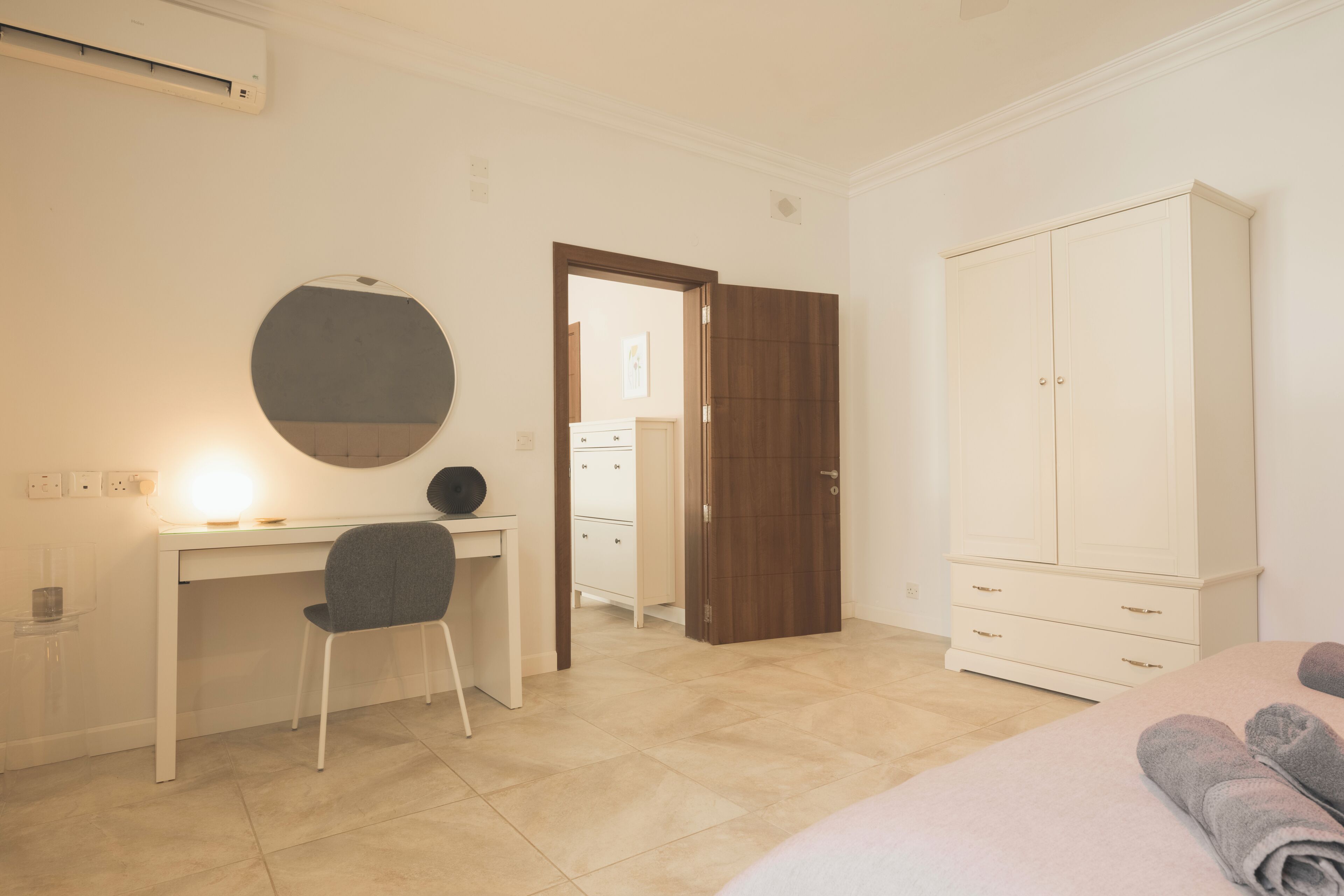 A bedroom with a bed, a desk, a chair, a wardrobe, and a door leading to another room.