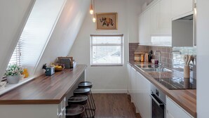 Eine Küche mit Holzausziehtisch, Barhocker, einem Fenster mit Jalousien und einer Hängelampe.