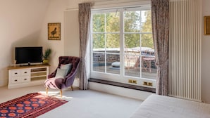 Ein Schlafzimmer mit einem Bett, einem Fernseher, einem Sessel, einem Fenster mit Vorhängen und einer Heizung.