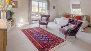 Ein Schlafzimmer mit einem Bett, zwei Sesseln, einem Fernseher, einem Fenster und Blick ins Freie.