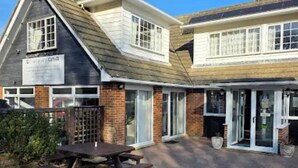 A building with a sign that reads 'Coastguard Inn,' a covered patio area, and a wooden picnic table. - Coastguard cafe room 2 (Hastings)