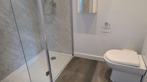 A bathroom with a glass shower enclosure, a toilet, and a marble-tiled wall. - Coastguard cafe room 2 (Hastings)