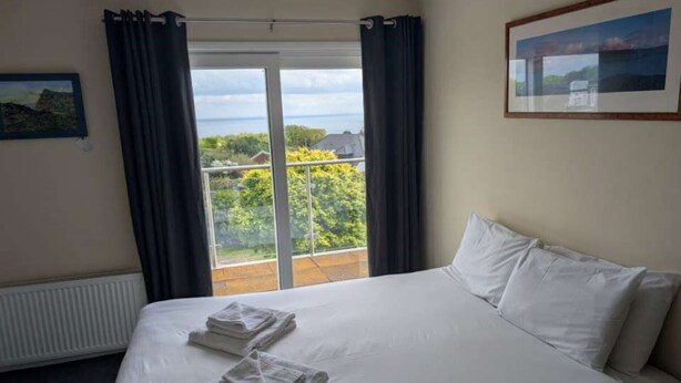 A hotel room with a bed, two towels, a window with curtains, a radiator, and a framed picture on the wall. - Coastguard cafe room 2 (Hastings)
