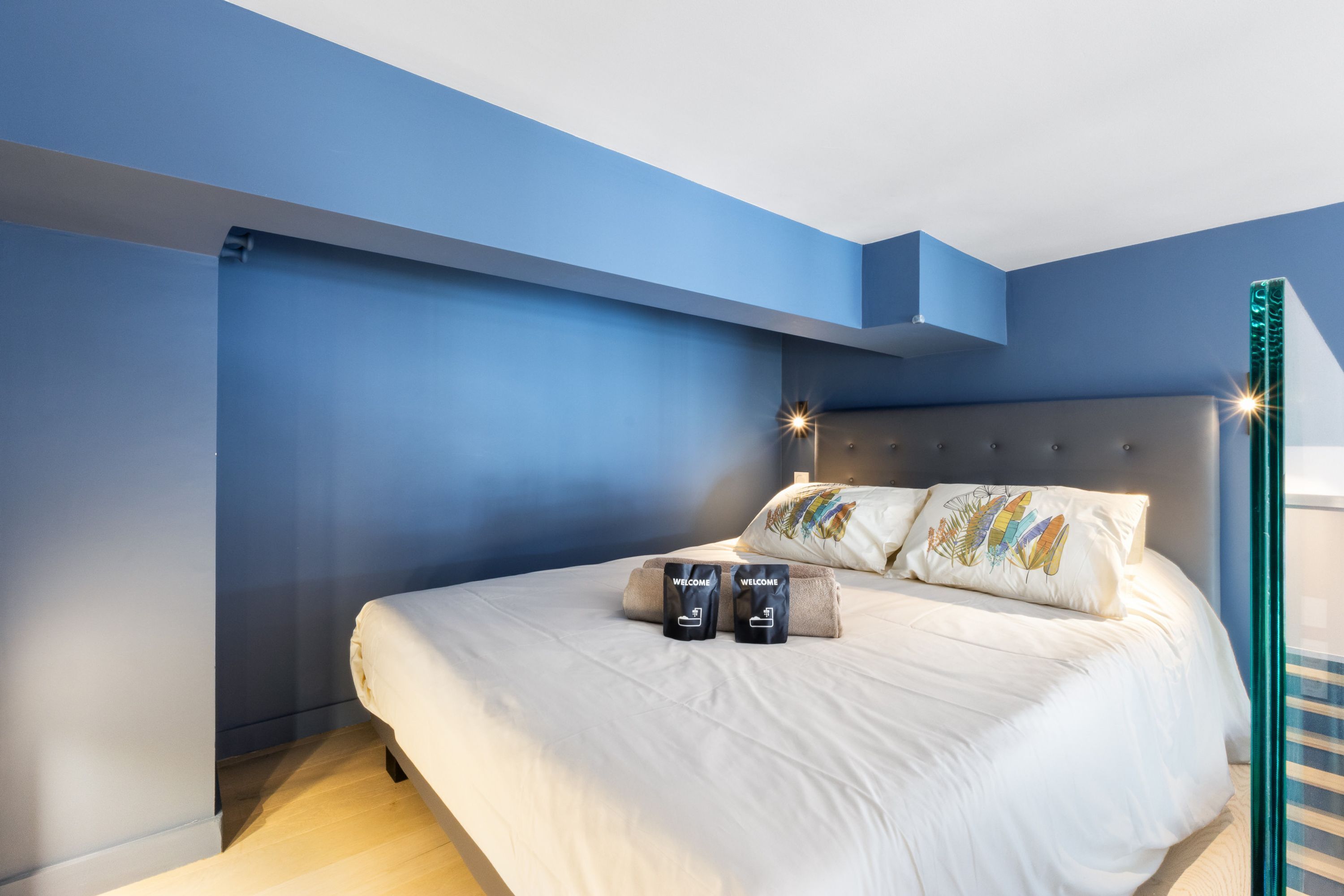 Un dormitorio moderno con una cama, dos almohadas y una mesita de noche con lámpara.