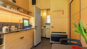 Une cuisine compacte équipée d’un évier, d’une bouilloire et d’ustensiles, un coin repas avec une table et des chaises, et une vue sur la salle de bain adjacente.