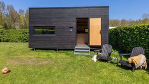 Un bâtiment moderne aux couleurs sombres, doté d’une cuisine ouverte, d’une porte et d’un petit espace extérieur aménagé avec des chaises et une table.