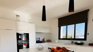 Una cucina moderna con mobili bianchi, un'isola in marmo, sgabelli di legno e luci a sospensione.