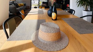 Un soggiorno moderno con zona pranzo, che include un tavolo di legno grande, sottopiatti intrecciati, una bottiglia di vino e una pianta in vaso.