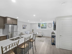 A modern kitchen with a central island, stainless steel appliances, and a dining area with chairs. - Cozy Retreat - Home Away From Home (Calgary)