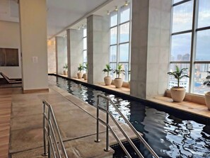 Piscina com vista para a cidade, janelas amplas e plantas em vasos.
