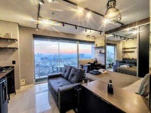 Uma sala de estar moderna com uma janela grande, um sofá, uma mesa de centro e uma área de cozinha.