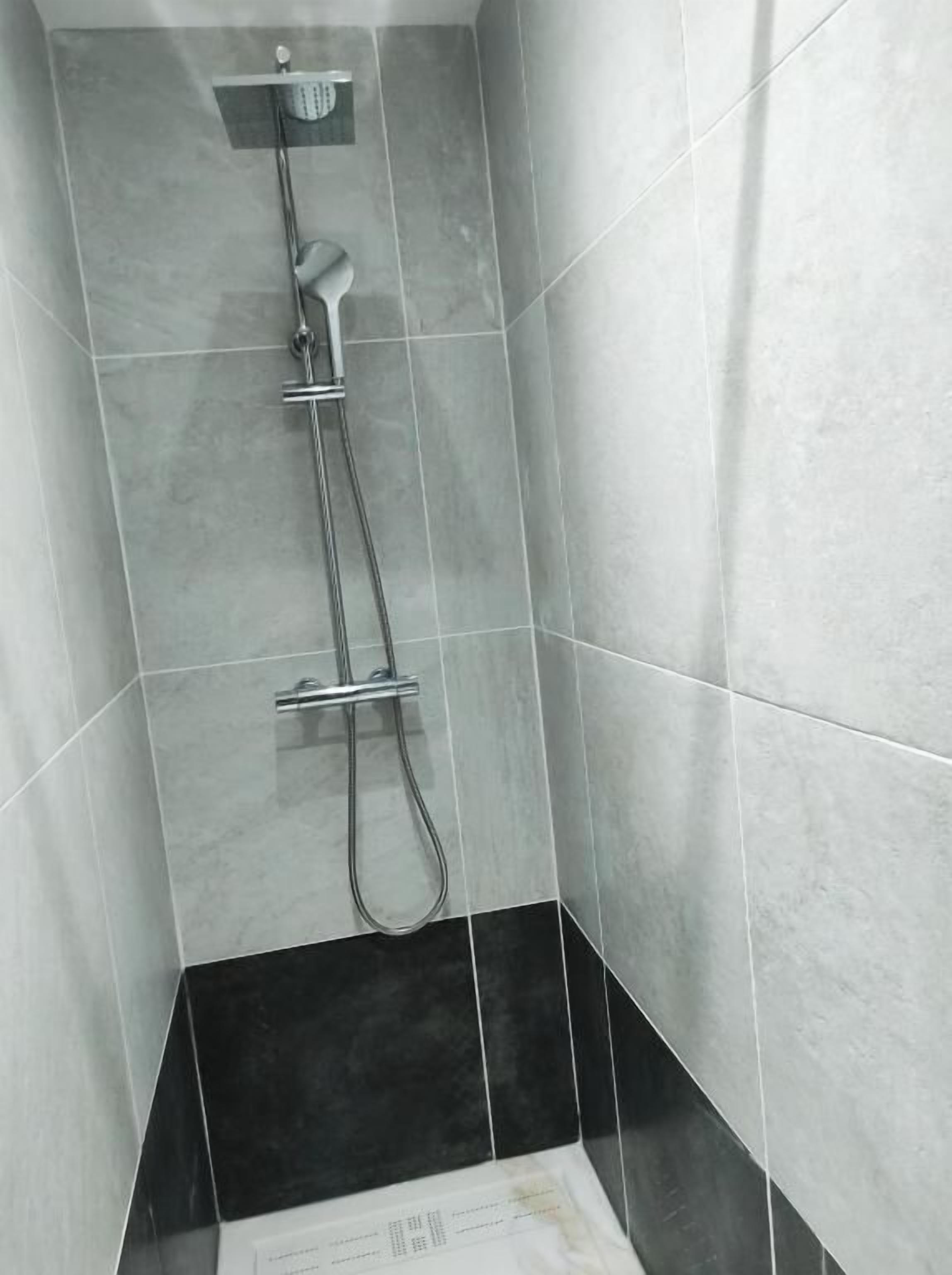 A shower with a handheld showerhead and a wall-mounted faucet.