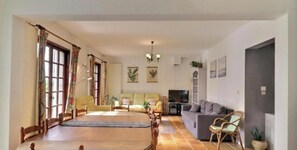 Ein Wohnzimmer mit einer Couch, Sesseln, einem Esstisch und einem Fernseher.