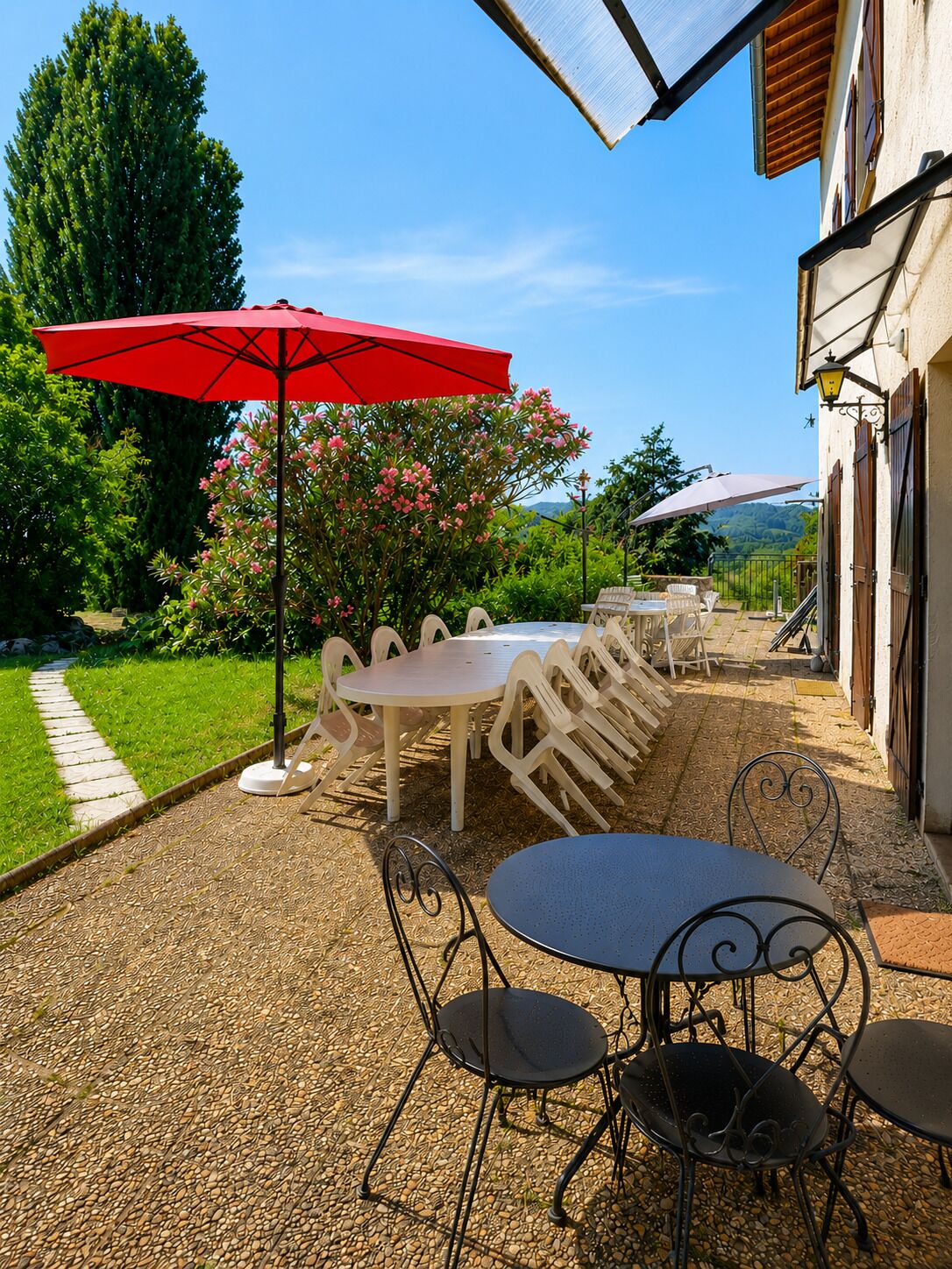 A patio with outdoor seating, a red umbrella, and a view of a building with a garden.