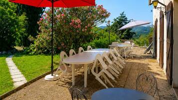 A patio with outdoor seating, a red umbrella, and a view of a building with a garden.