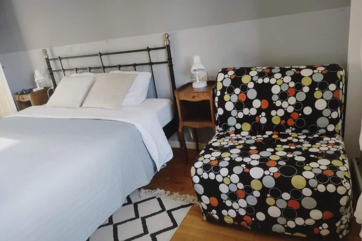 A bedroom with a bed, a nightstand, a lamp, and a polka-dotted chair.