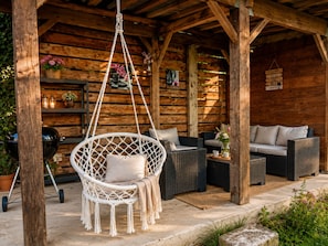 Una cabaña de madera con un sillón colgante, muebles de mimbre y una parrilla.