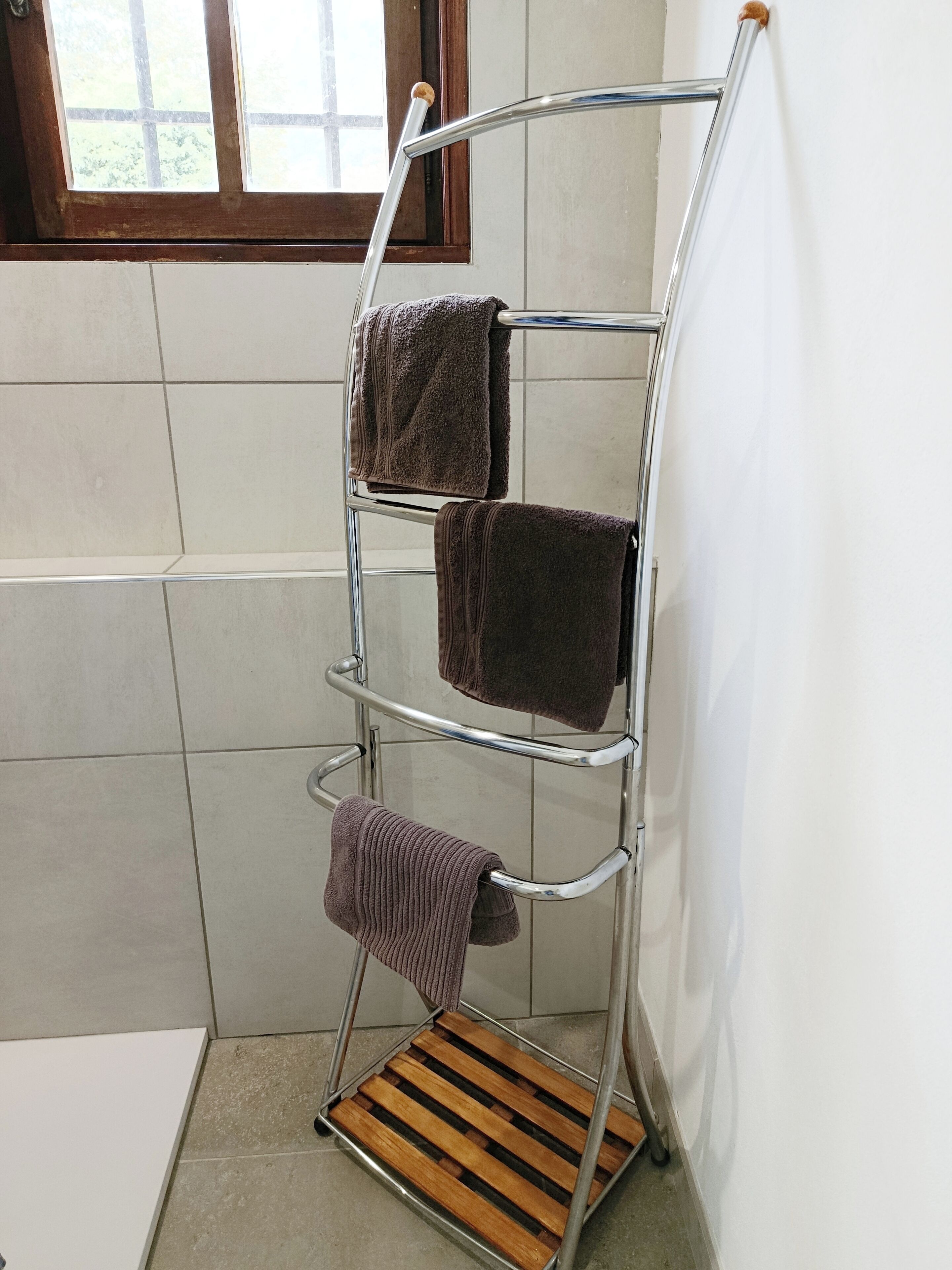 Un toallero de metal con tres toallas en un baño con paredes de azulejos y una ventana.