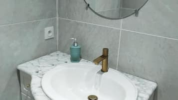 Un baño con lavamanos de mármol, grifo de bronce, espejo redondo y dispensador de jabón color aguamarina.
