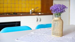 Una cocina con salpicadero de azulejos amarillos, un fregadero y una mesa con un florero tejido lleno de flores moradas.