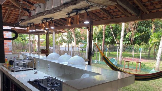 A kitchen with a gas stove, a long counter, and a view of a garden with a hammock. - Casa de Praia Na Ilha de Marajó - Joanes/PA (Salvaterra)
