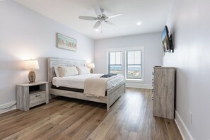 Ein Schlafzimmer mit Bett, Nachttischen, Deckenventilator, Fernseher und Fenster mit Blick.