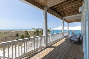 Eine Holzterrasse mit Geländer, ein blaues Gebäude und Blick auf den Strand.