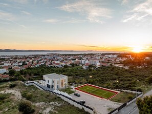 A residential area with a tennis court, surrounded by houses and greenery, during sunset. - Villa Odeona ZadarVillas (Zadar)