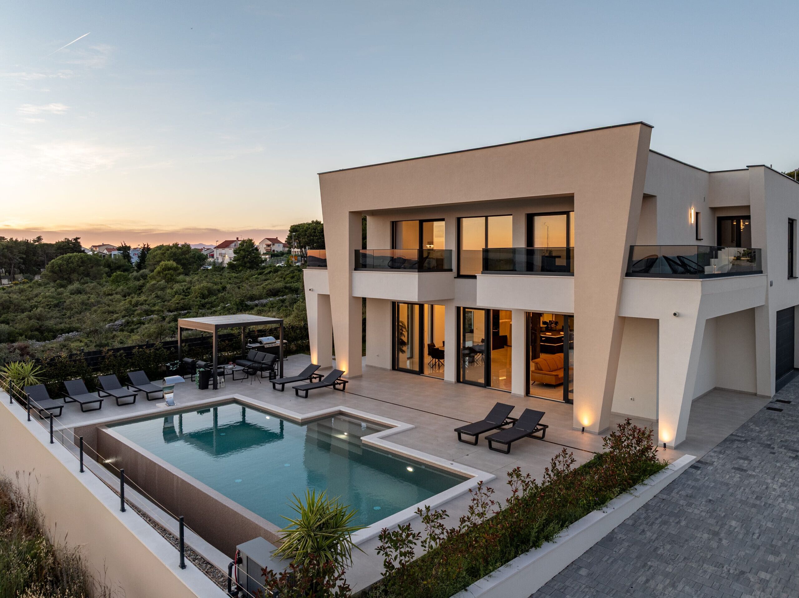 A modern two-story building with a swimming pool, outdoor seating, and a view of the surrounding landscape.