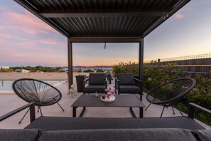 Una terraza en la azotea con piscina, mobiliario exterior y vistas a la ciudad al atardecer.