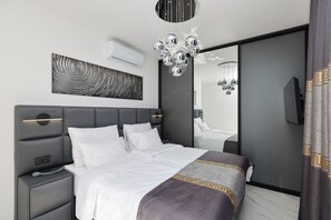 A modern bedroom with a grey headboard, white bedding, a decorative mirror, and a chandelier. - Villa Odeona ZadarVillas (Zadar)