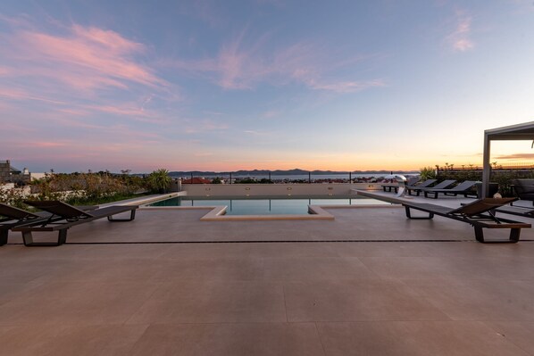 A rooftop pool area with lounge chairs and a view of the cityscape at sunset. - Villa Odeona ZadarVillas (Zadar)