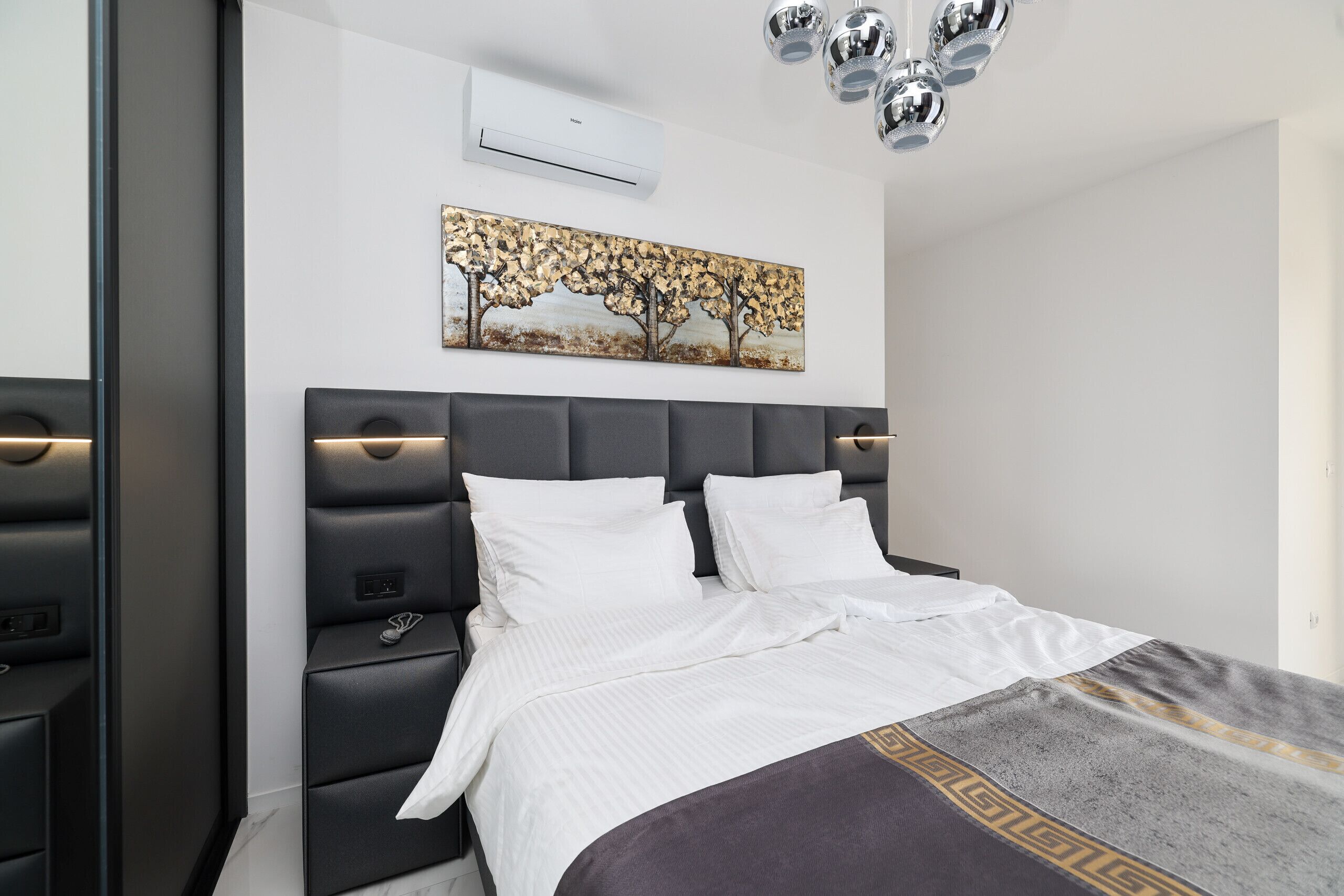 A modern bedroom with a bed, bedside tables, an air conditioner, and a ceiling light fixture.