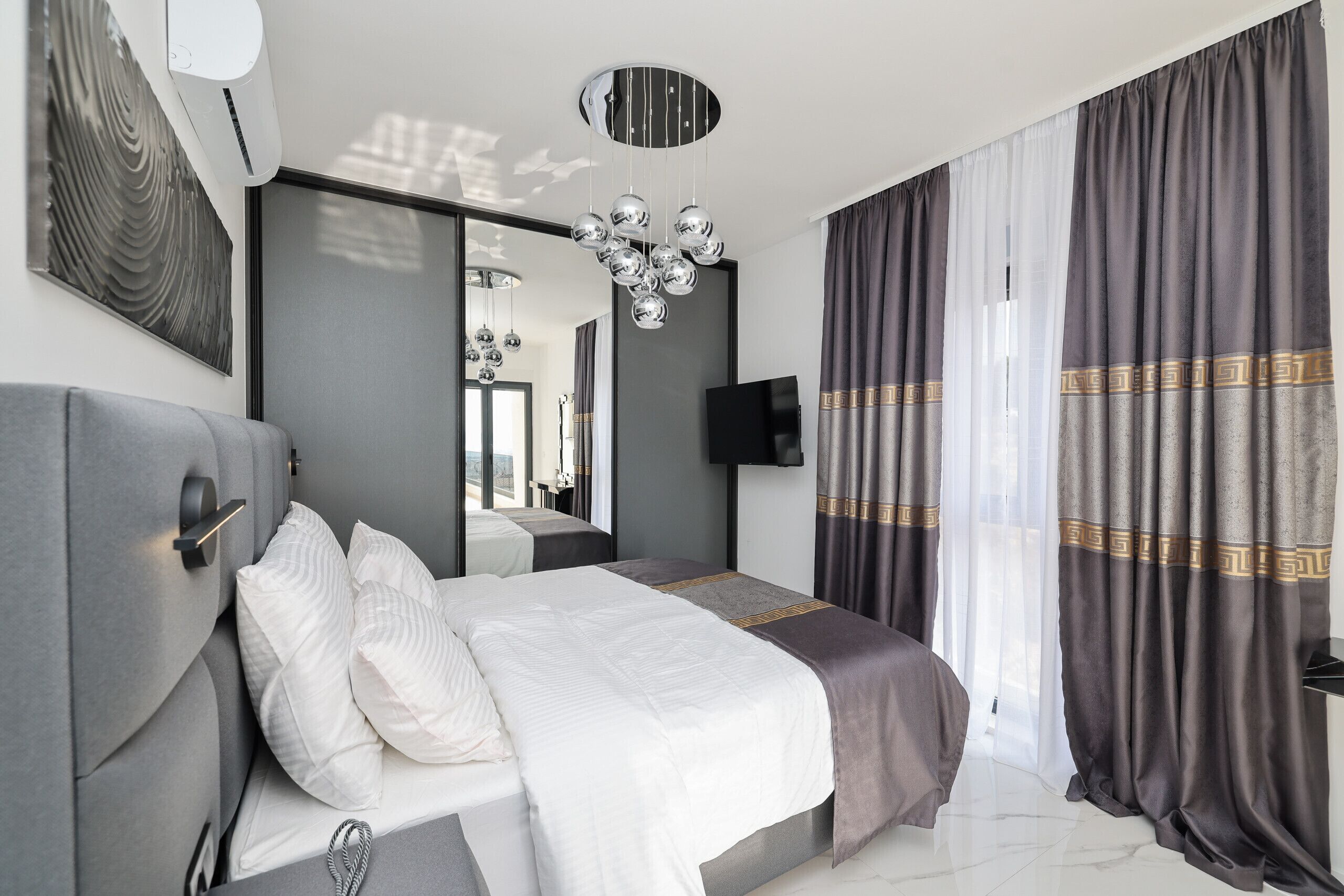 Une chambre moderne avec un grand lit, un téléviseur à écran plat, un luminaire au plafond et un grand miroir.