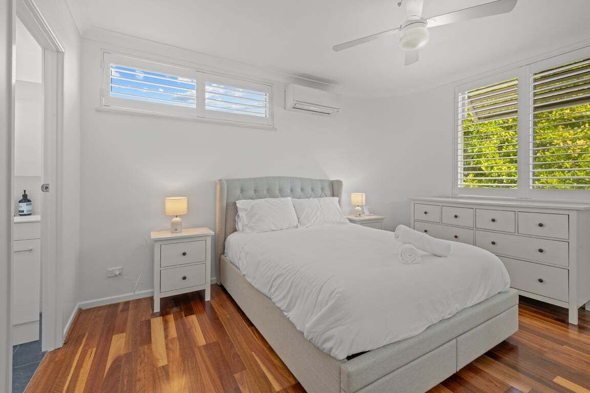 A bedroom with a bed, nightstands, a dresser, a ceiling fan, and a window with blinds.