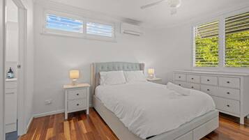 A bedroom with a bed, nightstands, a dresser, a ceiling fan, and a window with blinds.