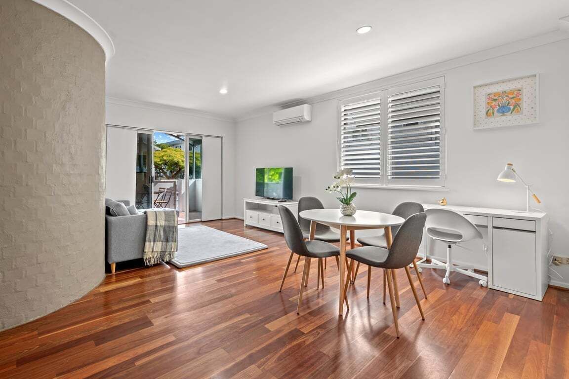 A modern living room with a dining area, a grey sofa, a TV, and a desk with a lamp.