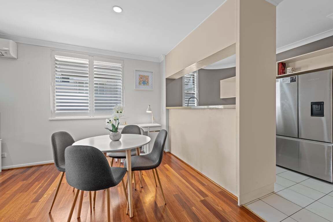 A modern kitchen with a built-in refrigerator, a dining area with a round table and chairs, and a window with blinds.